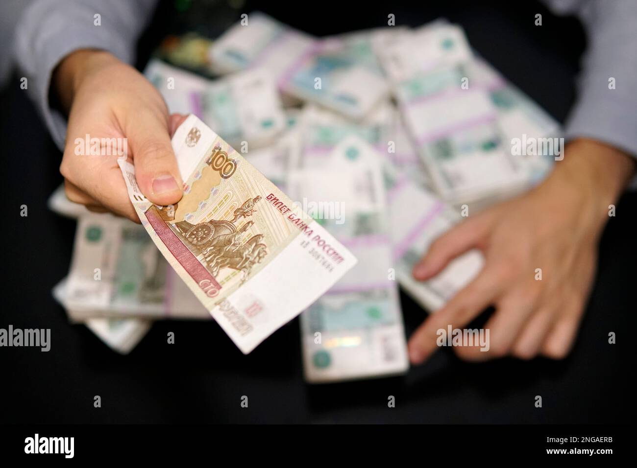 Der Mann hält einen Hundert-Dollar-Schein in russischen Rubeln und hält die Hände von Millionen Rubel. Das Konzept von Gier, Wucher oder Nächstenliebe. Stockfoto
