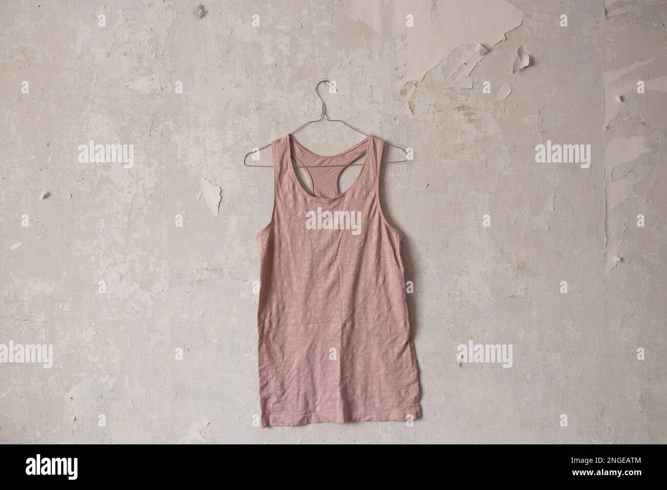 Pinkes T-Shirt, das an einem Kleiderbügel an einer alten, schmutzigen weißen Wand zu Hause hängt Stockfoto