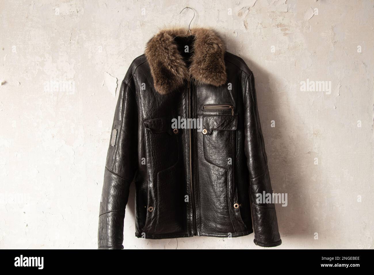 Schwarze Winterjacke aus Leder für Herren, die im Innenbereich an einem Kleiderbügel an der Wand hängt Stockfoto