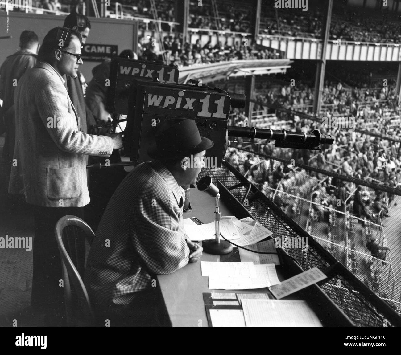 New York Yankees announcer Mel Allen, seated, reports the game between the Yankees and Baltimore Orioles from the television box behind home plate at Yankee Stadium on May 11, 1956. Behind the camera, center, is Jim Woods. (AP Photo/Robert Kradin) Stockfoto