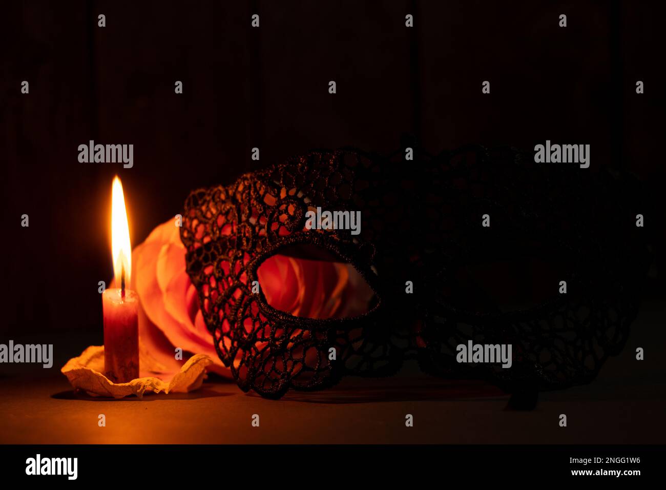 Eine Kerzenflamme und neben einer Rose in der dunklen Nahaufnahme Stockfoto