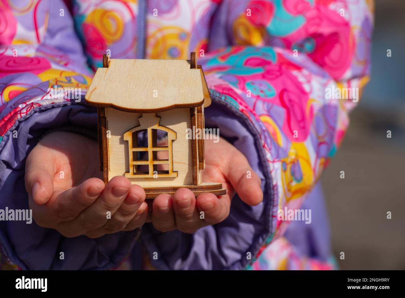 Die Kinderhand hält ein kleines Holzhaus auf einem verschwommenen Hintergrund Stockfoto