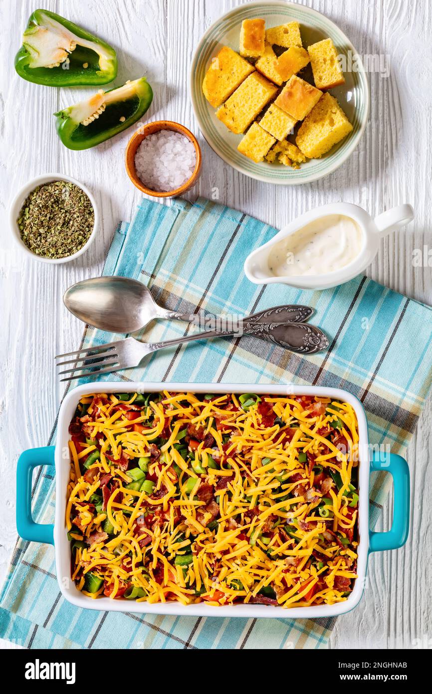 pinto Beans Speck Maisbrotsalat mit Tomaten, Paprika, Mais und Cheddar Käse in rechteckiger Schüssel auf weißem Holztisch mit Löffel und Gabel, vertica Stockfoto