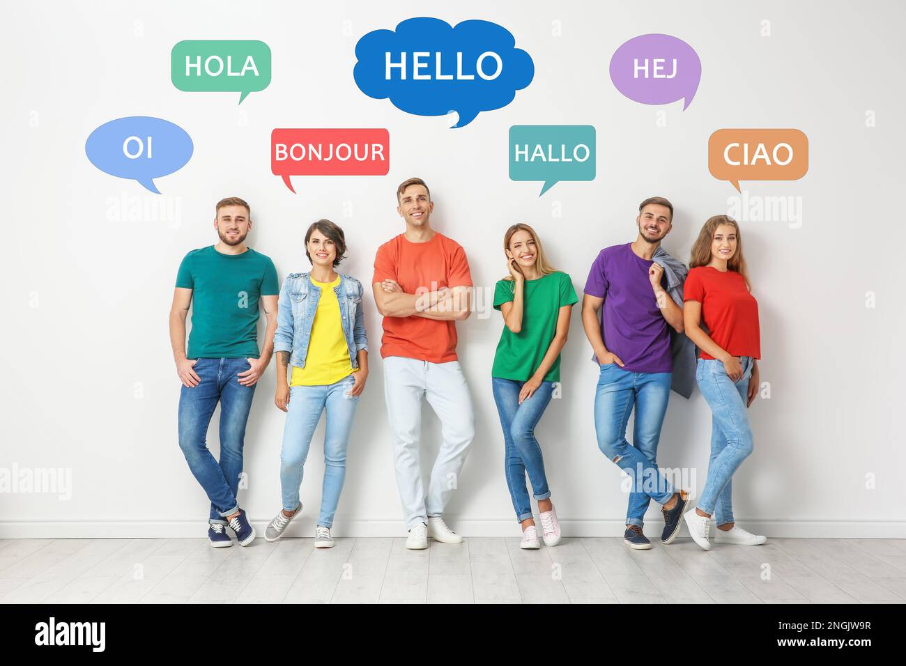 Fröhliche Leute, die neben einer hellen Wand posieren und Sprechblasen mit dem Wort „Hallo“ in verschiedenen Sprachen illustrieren Stockfoto