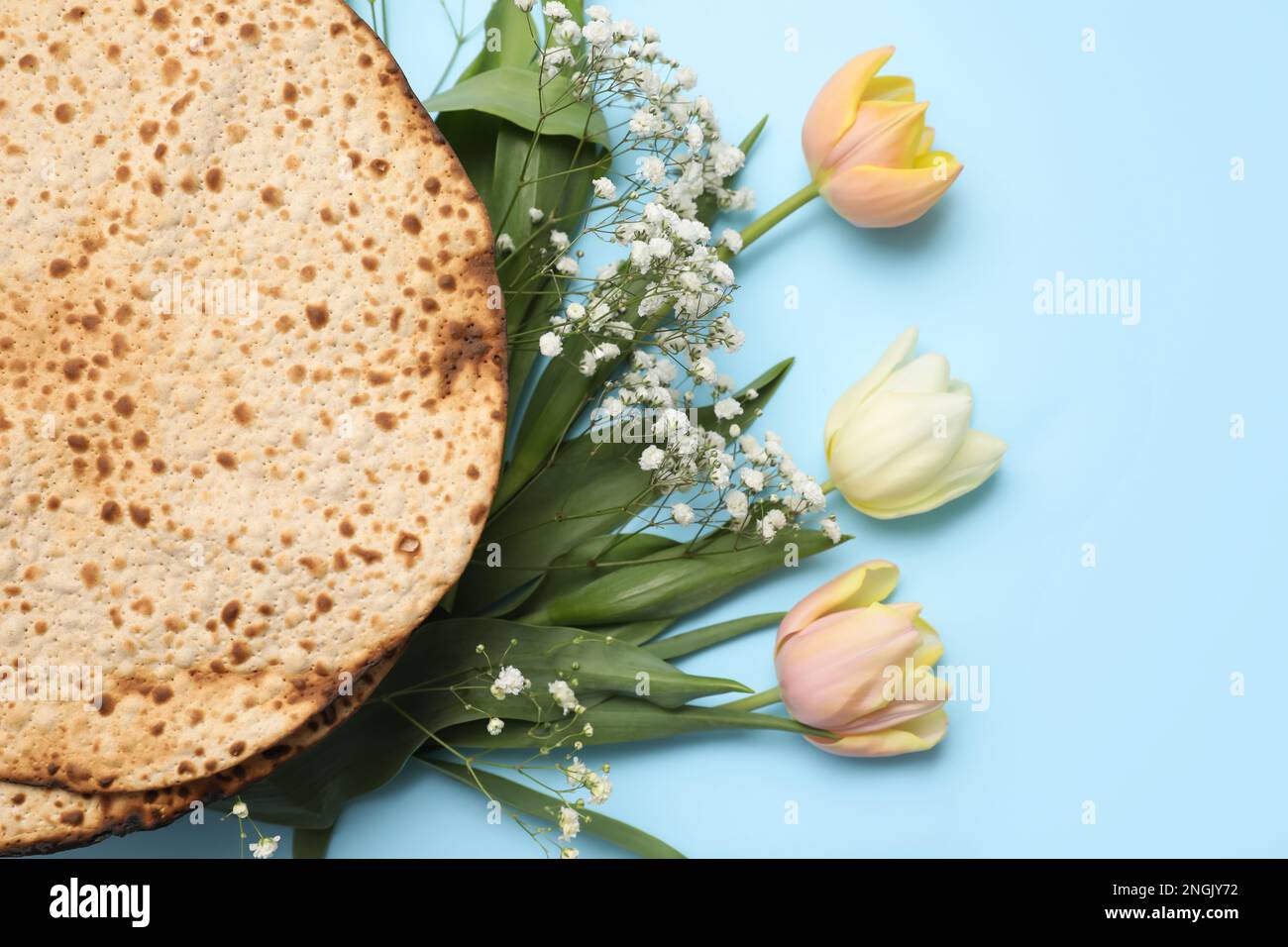 Leckere Matzen und frische Blumen auf hellblauem Hintergrund, flach liegend. Pessach-Feier Stockfoto