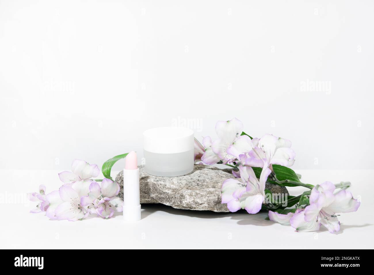 Weißer Kosmetikhintergrund. Kosmetikflaschen mit Blumenpflanze. Leere Etikettenverpackung für Branding-Modelle mit harten Schatten. Natürliches Organ Stockfoto