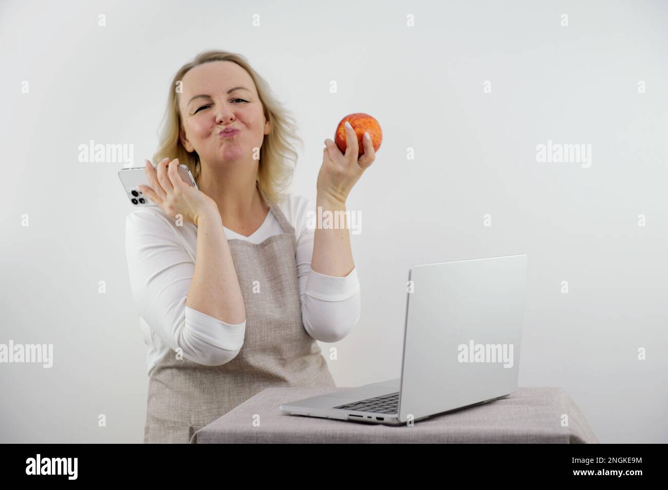 Schürze Telefon Laptop Foto einer schönen Frau, die ihr Smartphone benutzt, während sie Apfel isst, während sie zu Hause auf der Treppe sitzt. Hochwertiges Foto Stockfoto