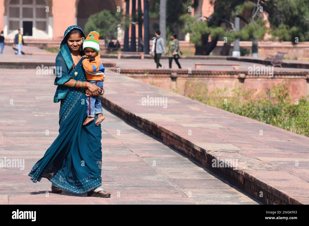 Eine junge indische Hindu-Frau, gekleidet in einem wunderschönen grünen, traditionellen Saree, hält ihren jungen, einjährigen Sohn vor einem öffentlichen Denkmal in Agra India. Stockfoto