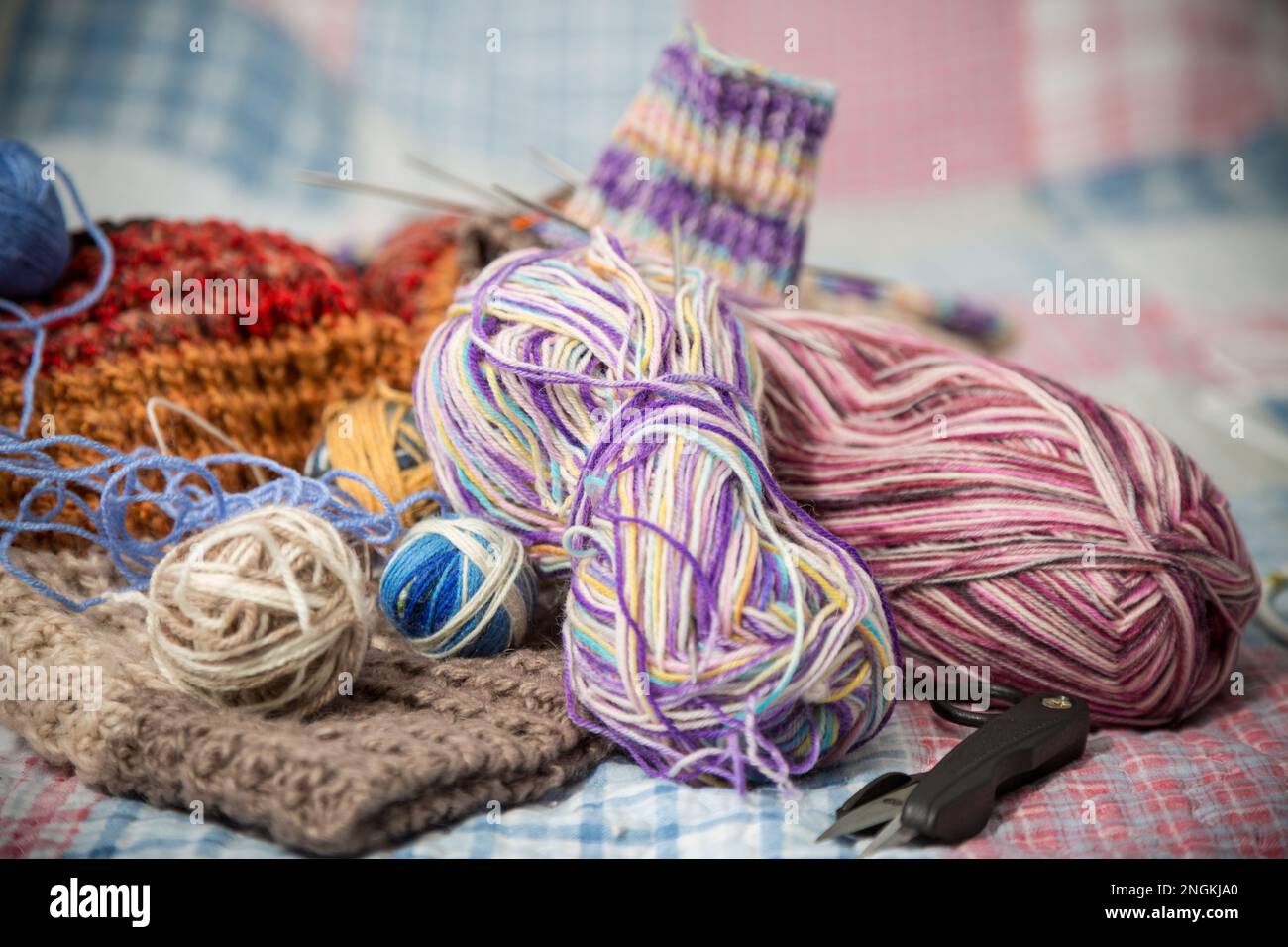 Farbige Fäden, Stricknadeln und andere Handstrickgegenstände auf dem Bett. Stockfoto