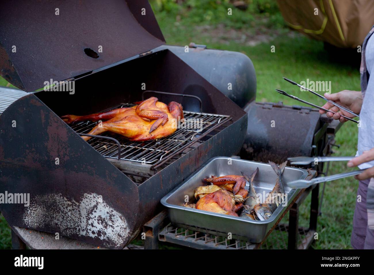 Seniorin grillt Hühnerfleisch für die Zubereitung des Essens im Camping, Senioren machen Freizeitaktivitäten und Freizeit-Picknick, während sie am Wochenende Fleisch braten, Stockfoto