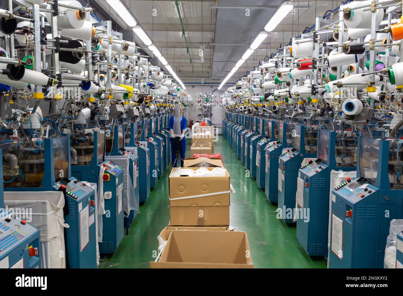 Textilindustrie mit Strickmaschinen in der Fabrik. Eine Mitarbeiterin führt eine visuelle Qualitätskontrolle der Strumpfwaren durch. Stockfoto