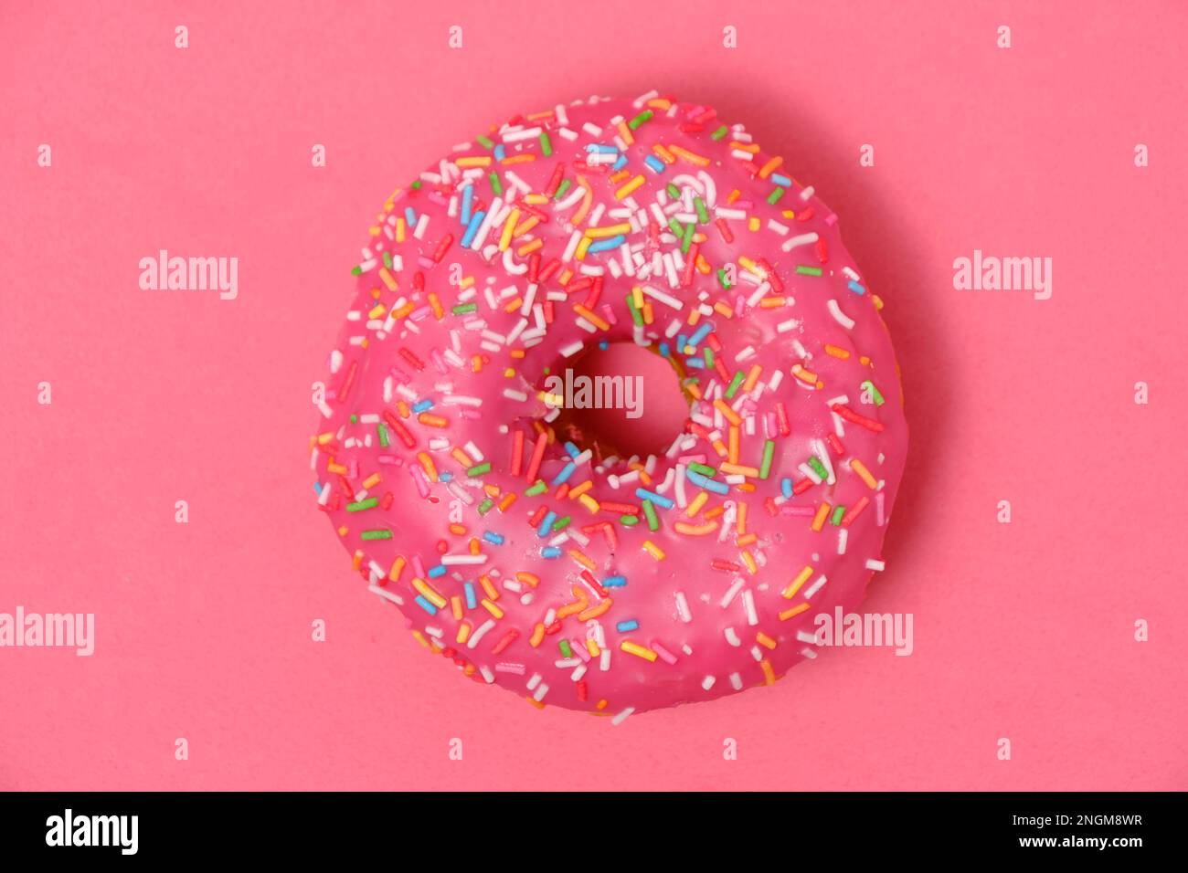 Donut mit pinkfarbenem Glasur und bunten Zuckerstreuseln. Auf pinkfarbenem Hintergrund Stockfoto