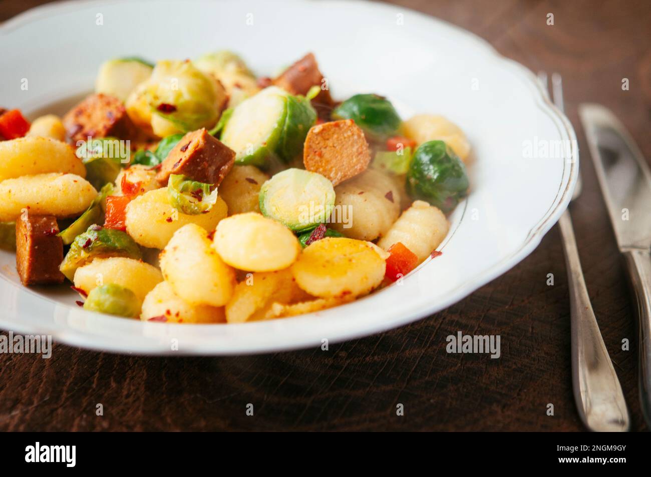 Platte mit Gnocchi, serviert mit Rosenkohl und vegane Hot-Dog-Stücke. Stockfoto