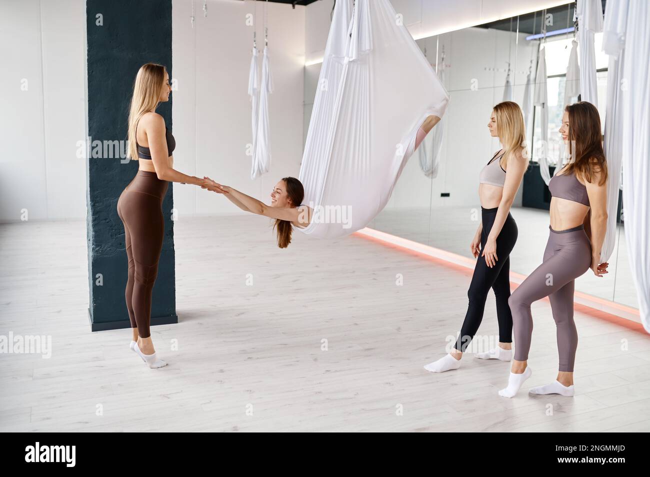 Junge Ausbilderin, die weibliche Gruppen-Stretching-Übungen an der Hängematte lehrt Stockfoto