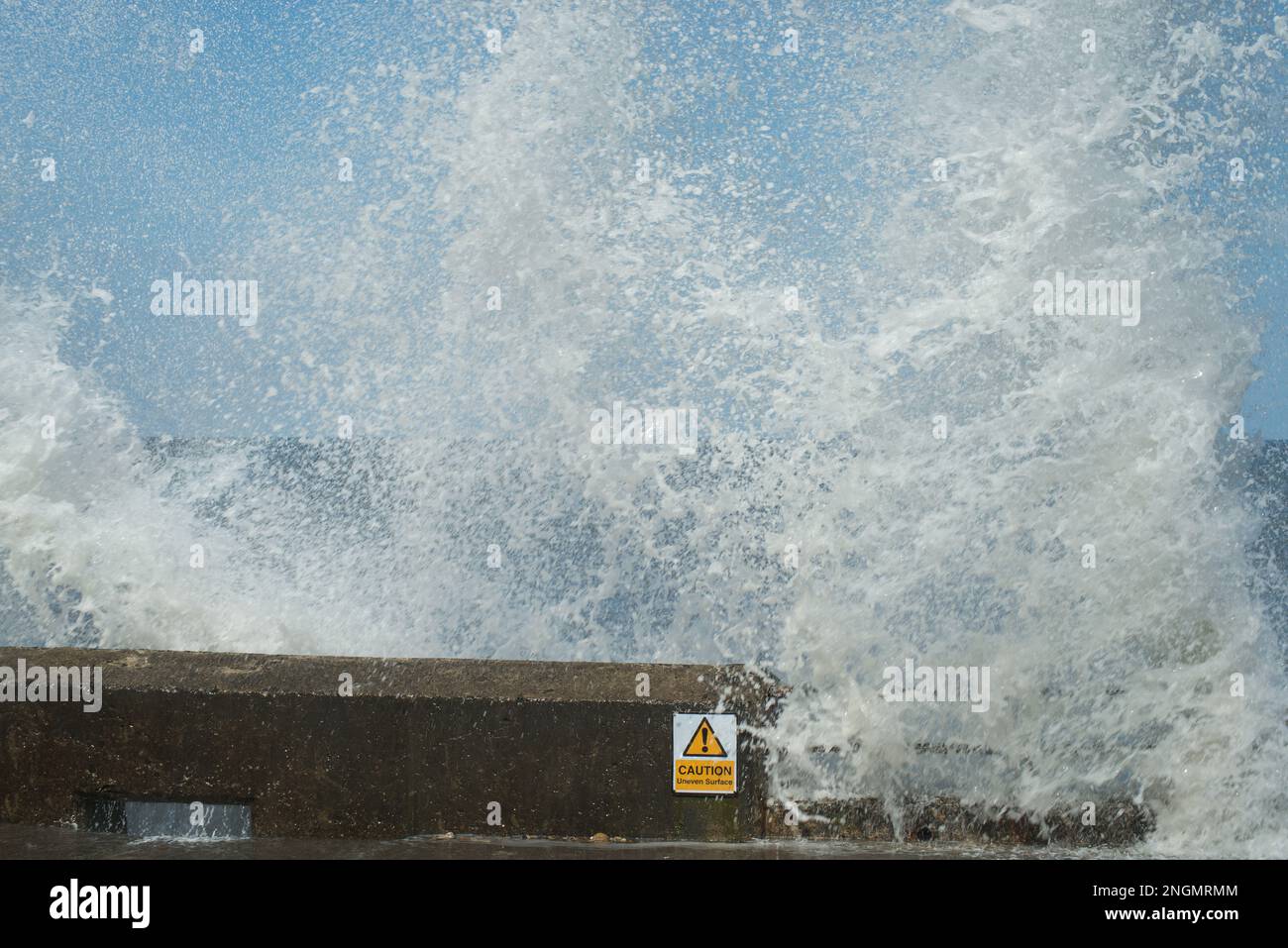 Stürzende Wellen werfen riesige Sprühsäulen hervor, die über die Betonpromenade platzen Stockfoto