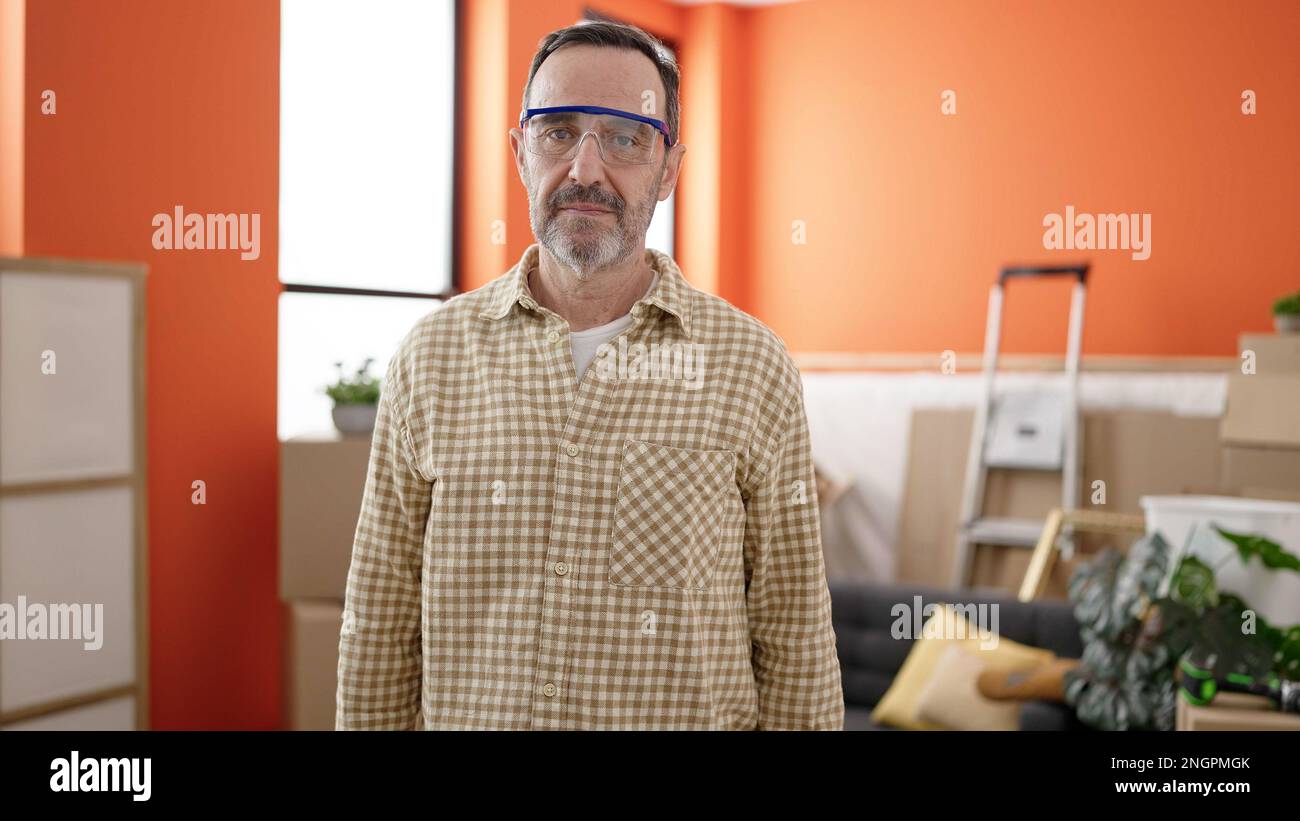 Ein Mann mittleren Alters, der eine Schutzbrille trägt, steht mit entspanntem Ausdruck im neuen Zuhause Stockfoto