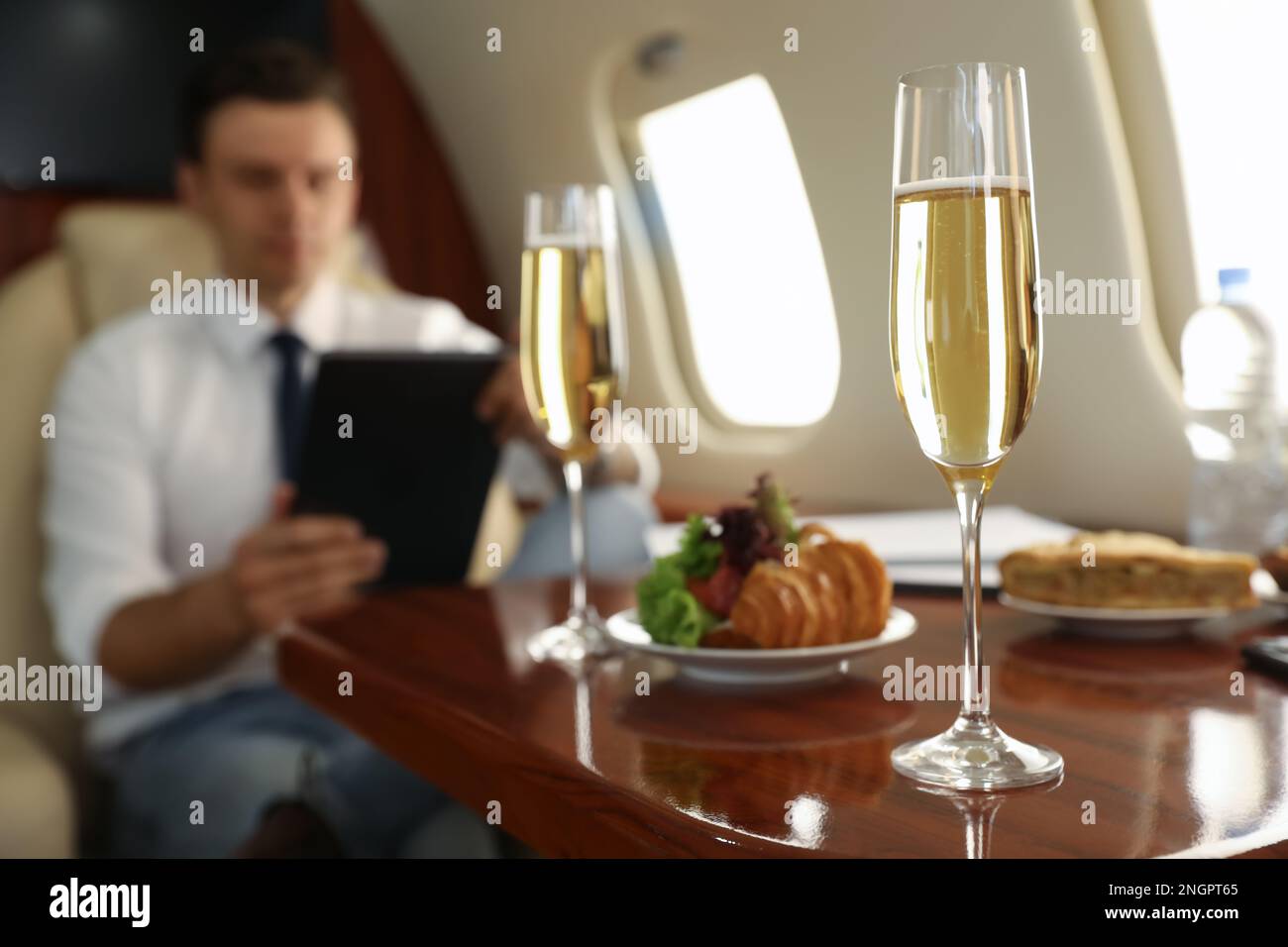 Geschäftsmann, der während des Fluges am Tisch im Flugzeug arbeitet, konzentriert sich auf ein Glas Champagner Stockfoto