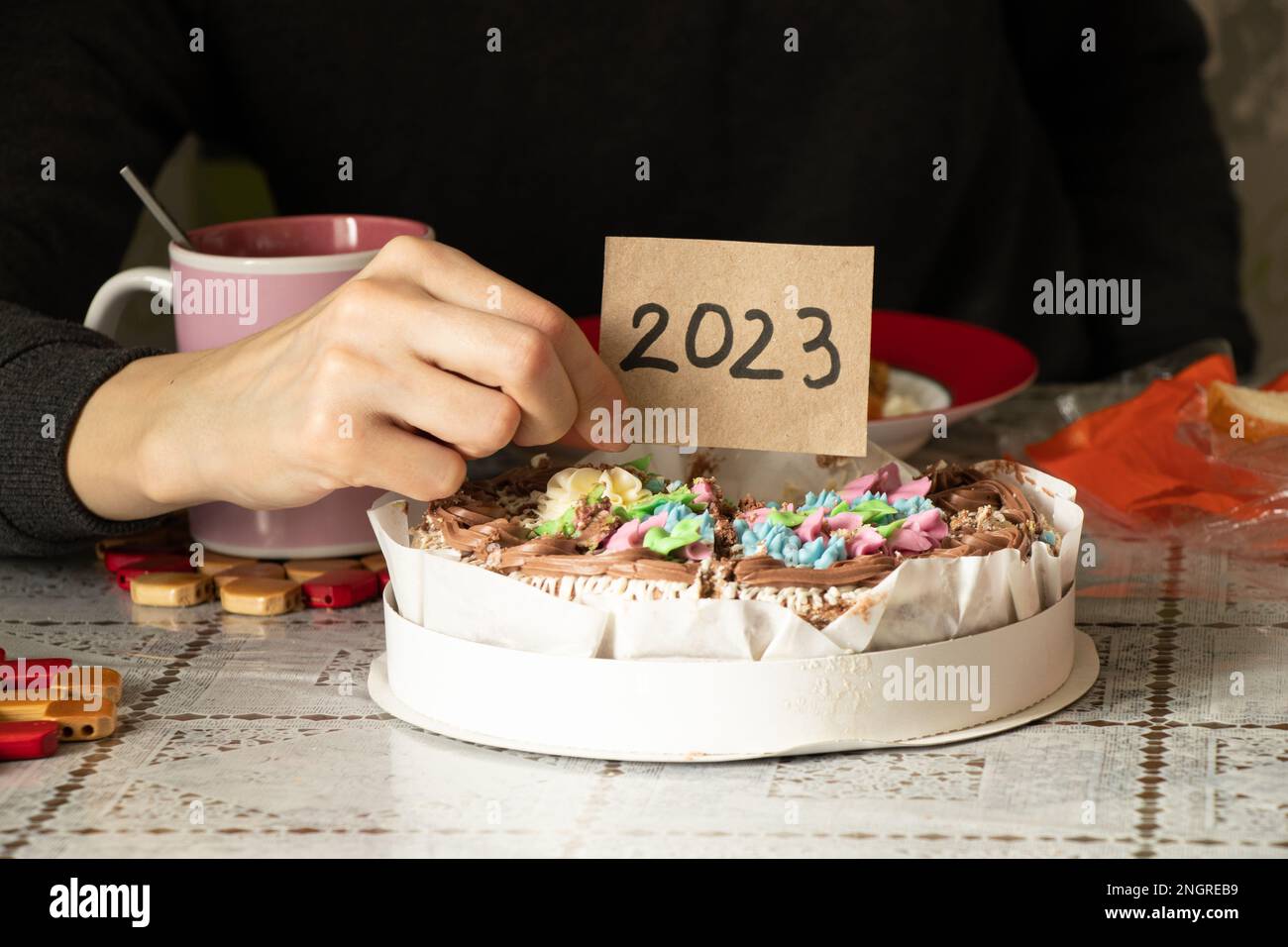 Ein Mädchen hält eine Karte mit dem Text 2023 über einem Kuchen und neben einer Tasse Kaffee in der Küche zu Hause, feiern Sie das neue Jahr 2023 Stockfoto