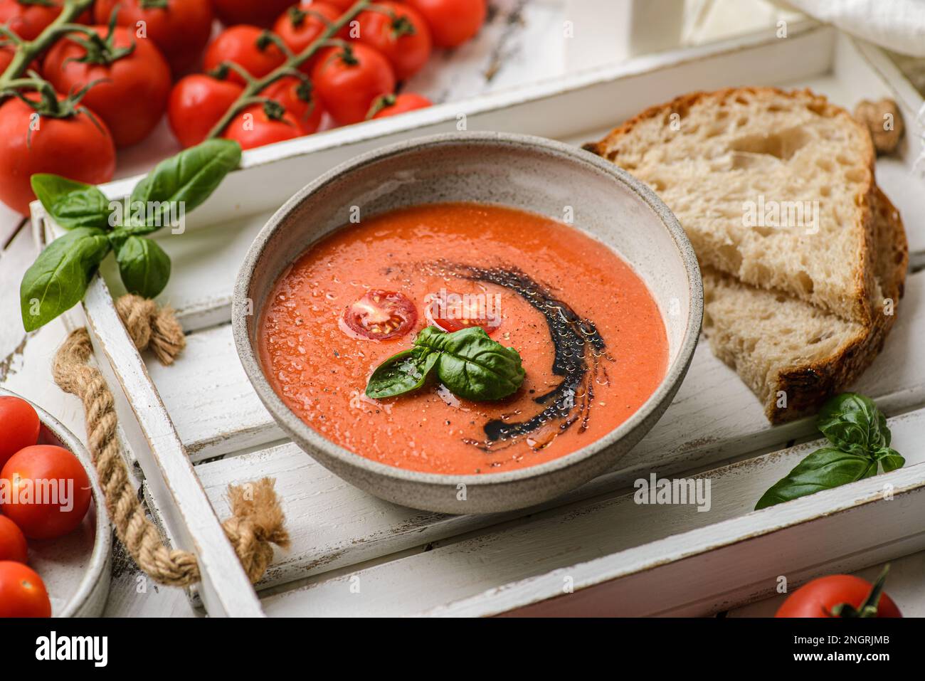Die Suppe besteht aus Tomaten, Paprika und Zwiebeln, dekoriert mit Tropfen Olivenöl und Basilikum. Es gibt Brot und Tomaten in der Nähe Stockfoto