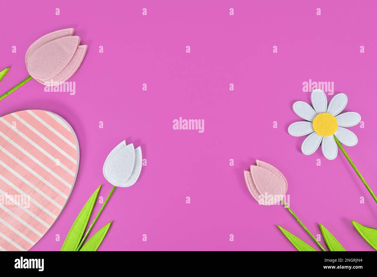 Tulpen- und Gänseblümchen-Frühlingsblumen und hölzerne Ostereier auf lila Hintergrund Stockfoto