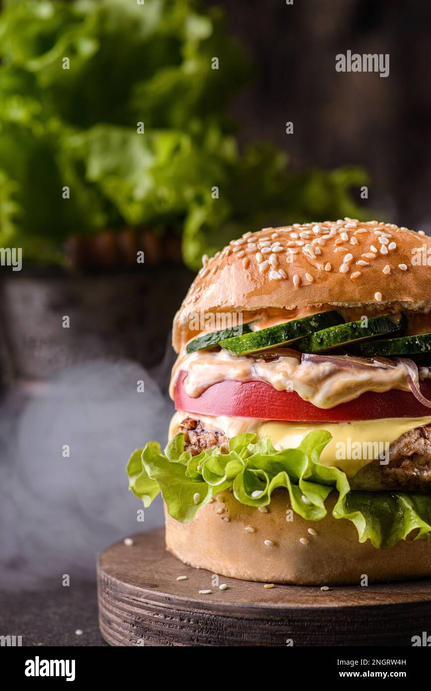 Burger auf einem Holzbrett, neben Rauch und Salat in einem Topf Stockfoto