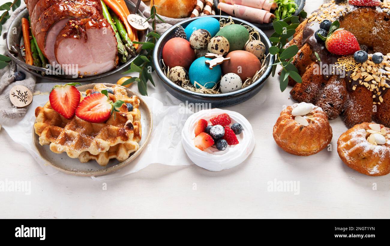 Traditionelles Osterabendessen oder Brunch mit Schinken, bunten Eiern, warmen Brötchen, Kuchen und Gemüse. Ostergerichte mit holtagstauglichen Dekorationen. Stockfoto