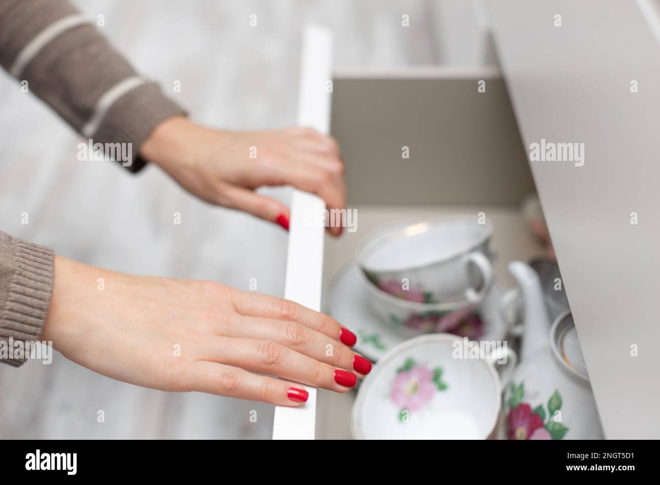 Eine Frau öffnet eine Schublade mit Teeutensilien. Eine Frau öffnet eine Schublade mit Utensilien. Schublade mit Küchenutensilien Stockfoto