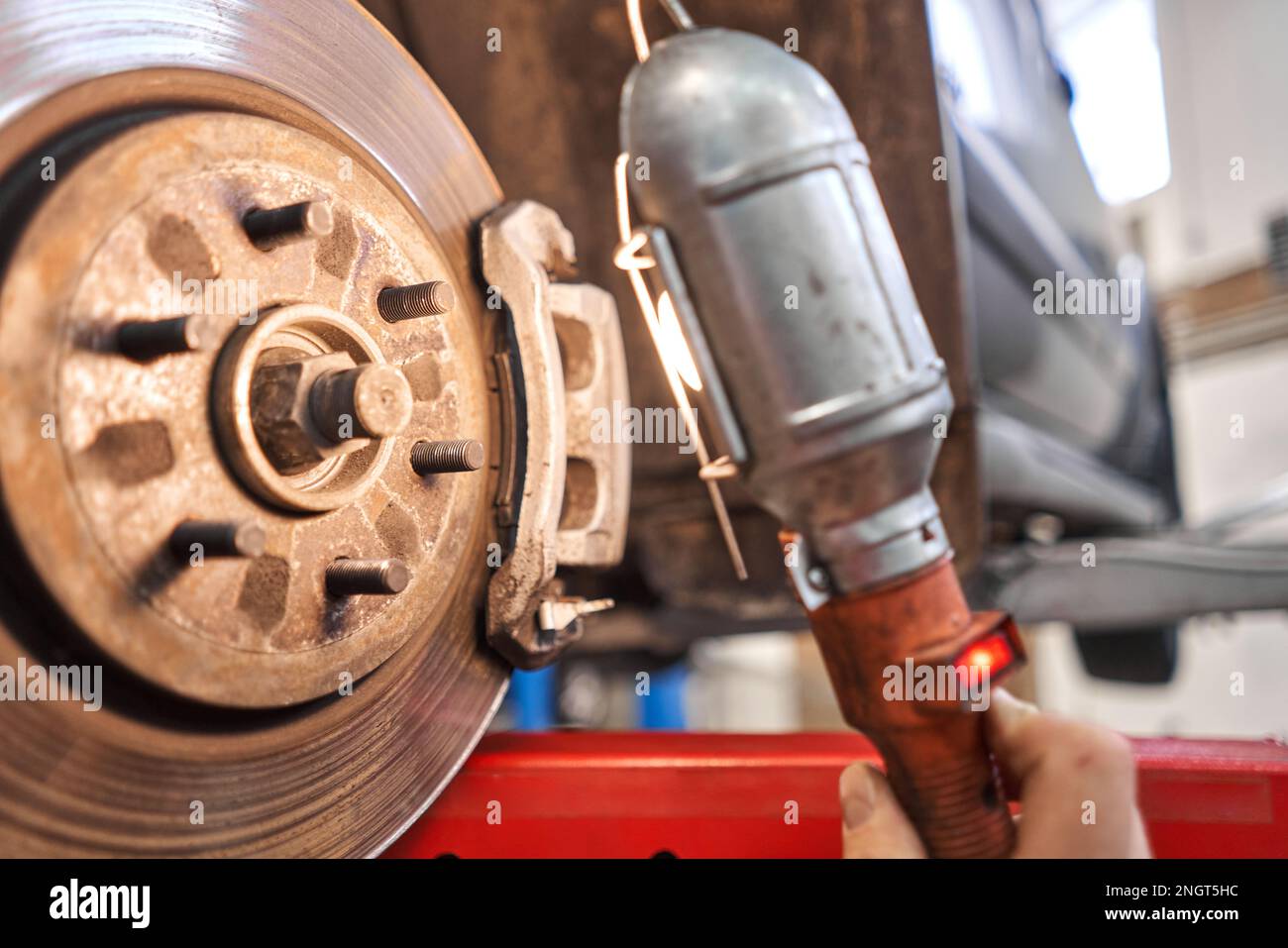 Ein Automechaniker inspiziert Bremsscheiben und Bremsbeläge mit einer Taschenlampe. Auto auf einem Reparaturständer. Technische Servicestation für Auto. Stockfoto