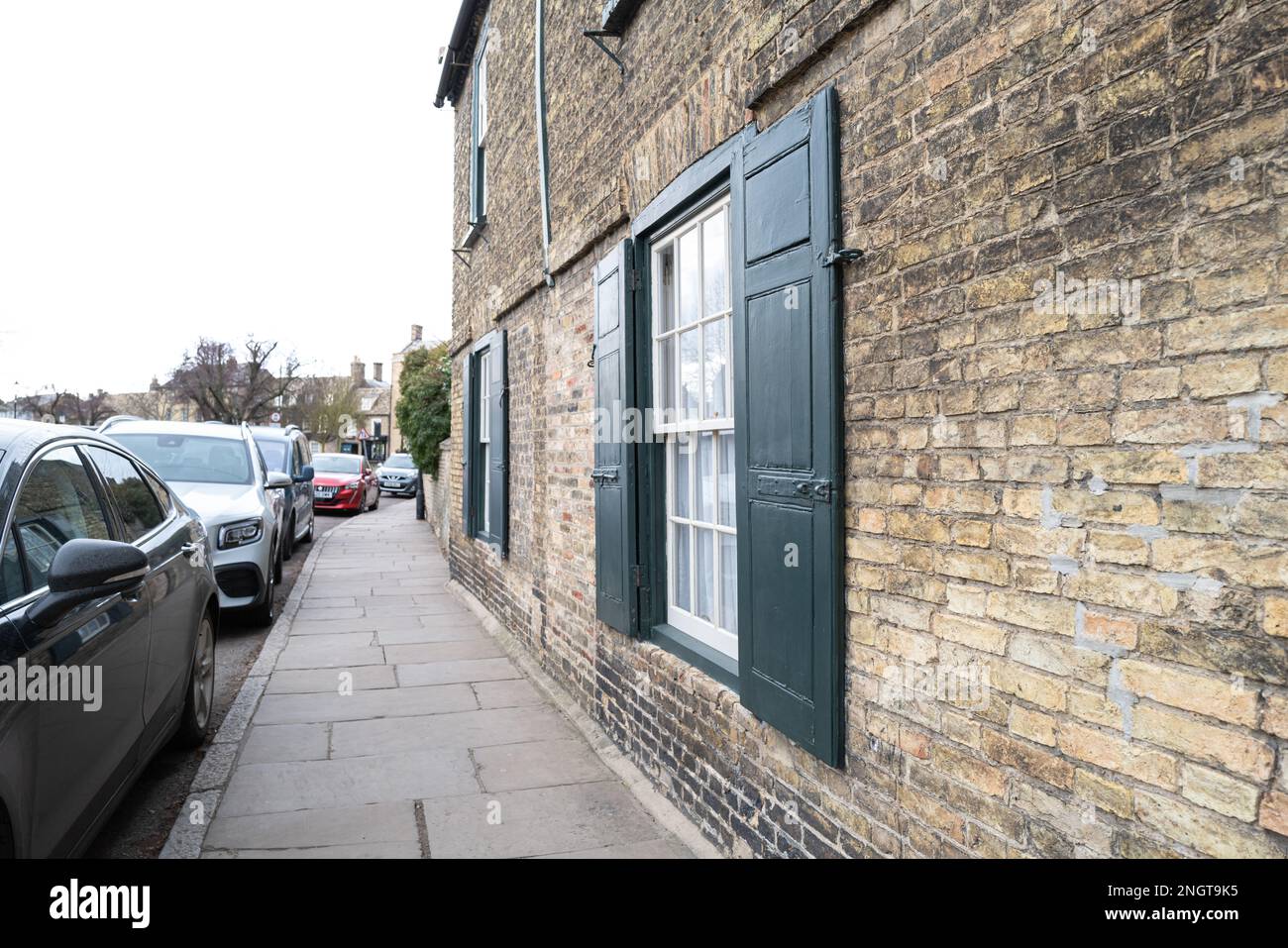 Große Fensterläden in einer engen, historischen Straße. Geparkte Autos sammeln sich am Markttag in der Gegend an. Stockfoto