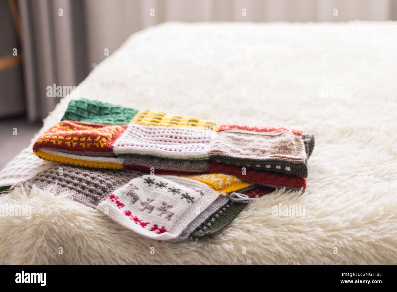 Warme Strickdecke auf dem Bett. Wollgemälde auf weißem Sofa. Karomuster. Gemütliche Zimmereinrichtung. Zimmer im Hygge-Stil. Strickhobby. Wintergemütlichkeit. Stockfoto