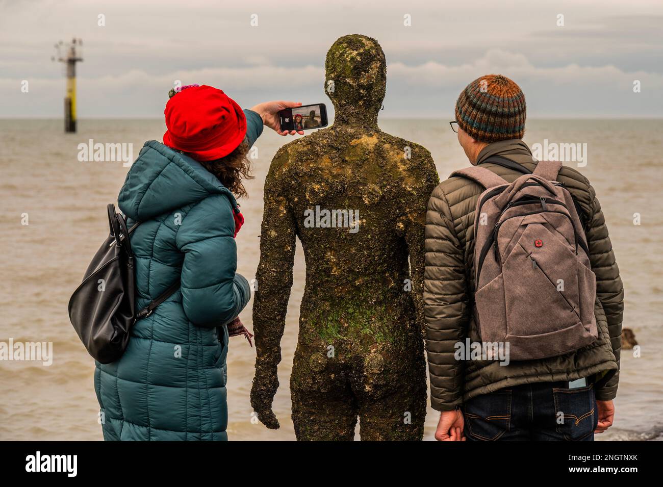 Margate, Großbritannien. 18. Februar 2023 Besucher besuchen Antony Gormley: Ein anderes Mal, am Nayland Rock, neben dem Turner Contemporary, in Margate. Das Werk wird erst enthüllt, wenn die Flut zurückgeht. Es ist eine von hundert soliden gusseisernen Figuren von Antony Gormley, die die Erfahrung des menschlichen Wesens erforschen. Leben an der Margate Küste. Kredit: Guy Bell/Alamy Live News Stockfoto