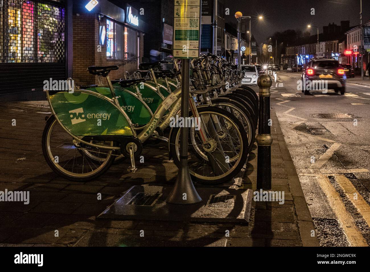 Geparkte Reihe von Leihfahrrädern in einer Vorstadtstraße in Cardiff, Wales bei Nacht Stockfoto