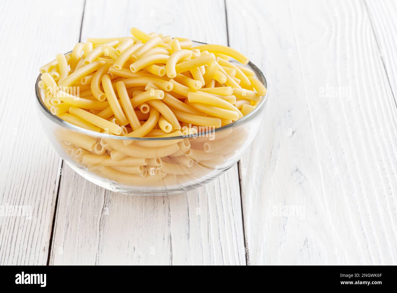 Ungekochte Makcheroni-Pasta in Glasschale auf weißem Holzhintergrund Stockfoto