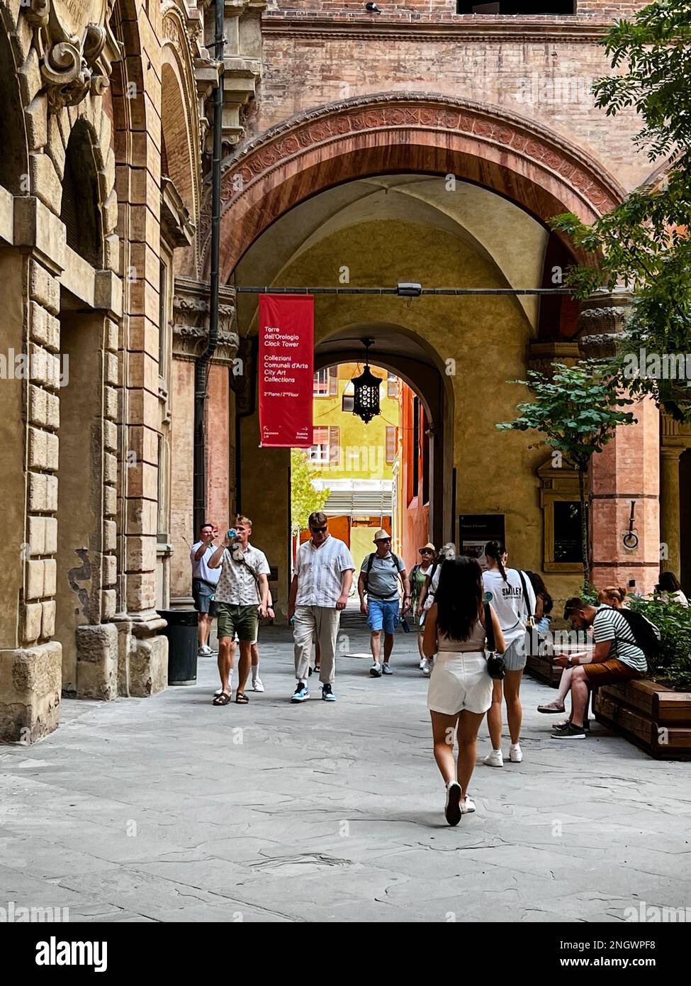 Touristenspaziergang entlang der Piazxza Maggiore in Richtung eines Torbogens, der zum Palazzo d'Accursio und Torre dell'Orologio in Bologna, Italien führt Stockfoto