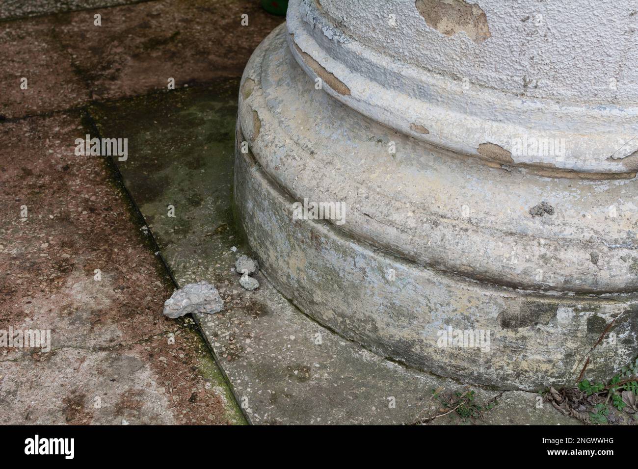 Alte Spaltenbasis. Fragment der Basis einer gerissenen Säule, gerissener Putz, Moos auf der Basis der Säule Stockfoto