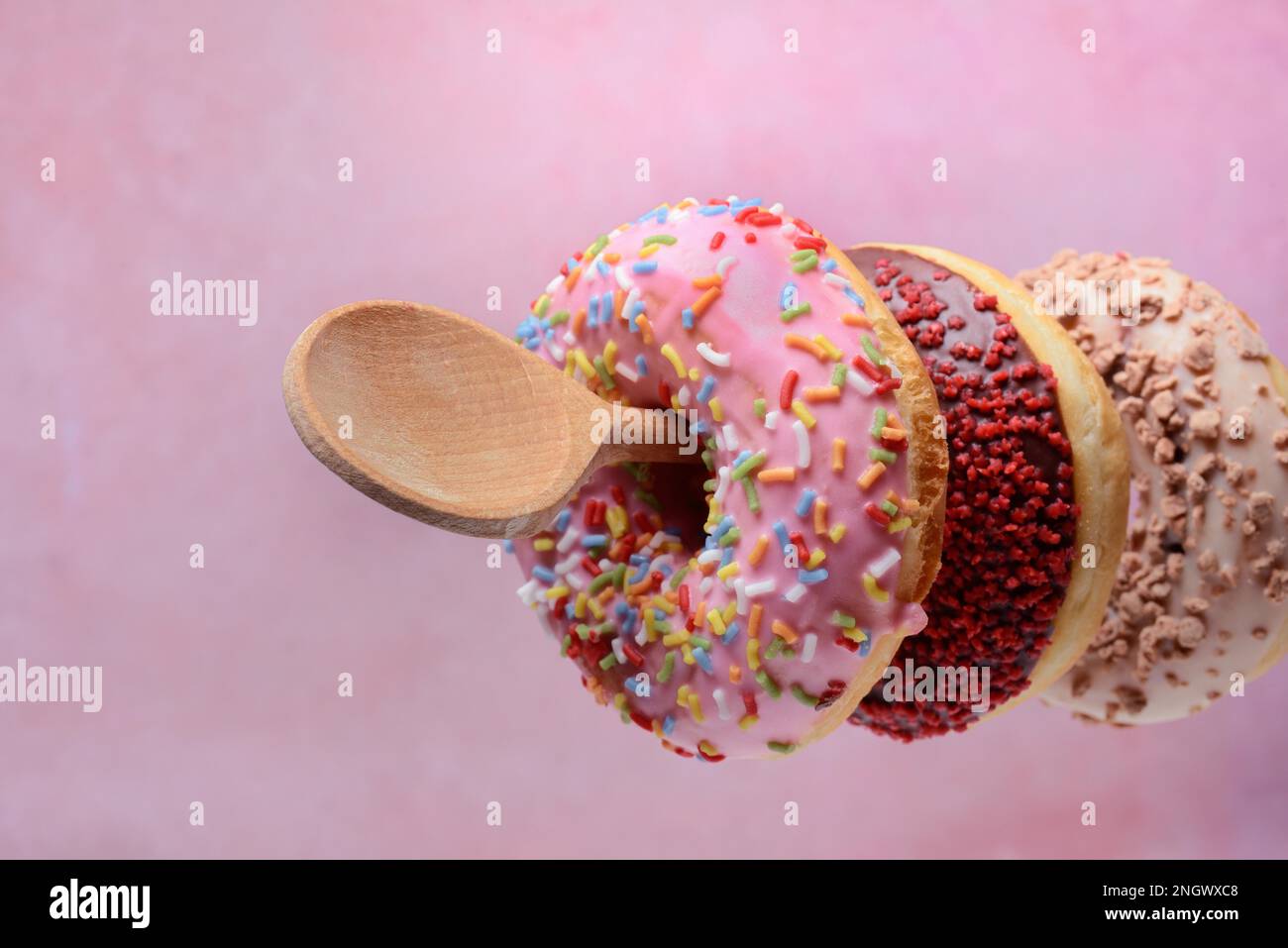 Donuts auf Holzlöffeln auf pinkfarbenem Hintergrund Stockfoto