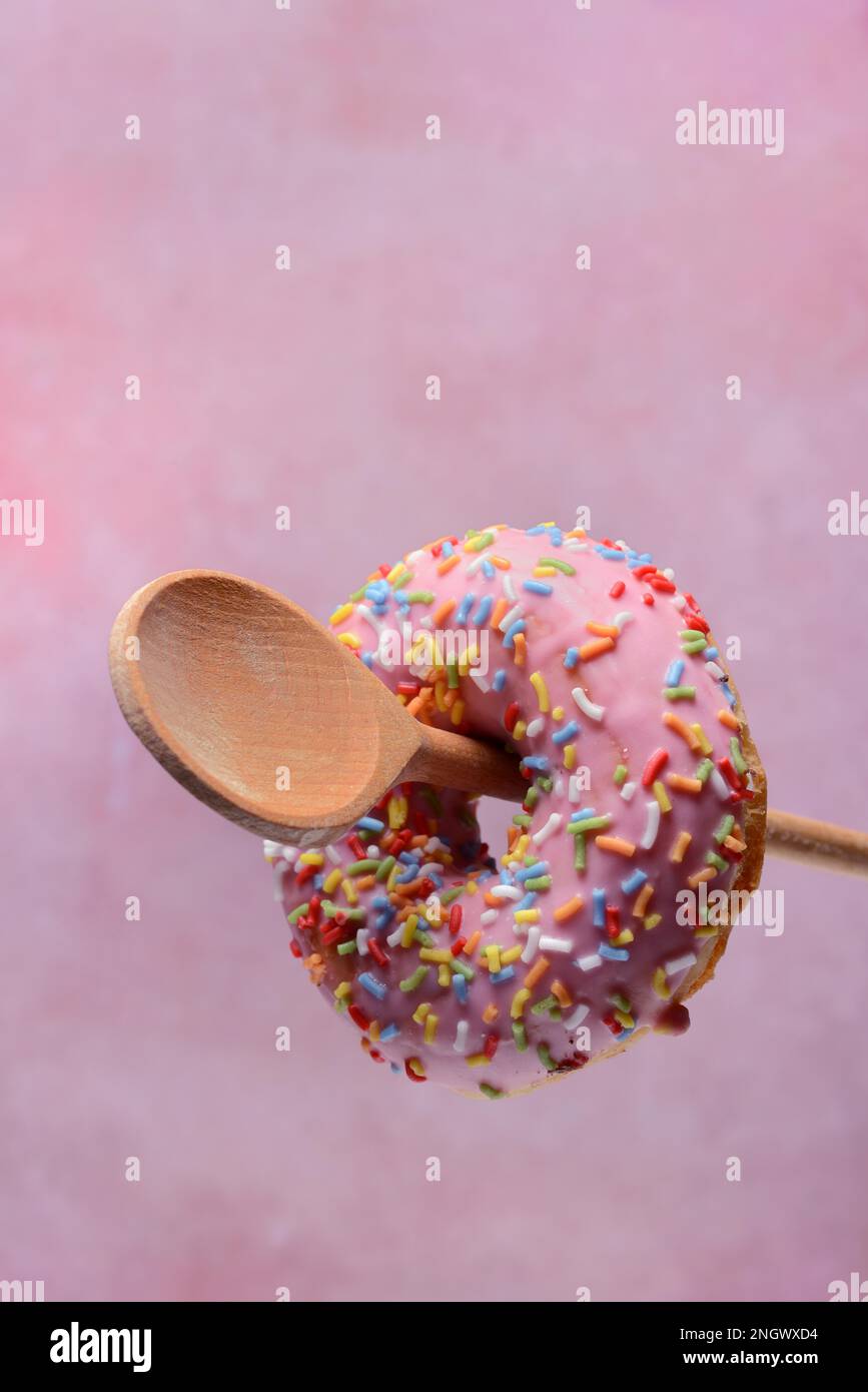 Donut auf Holzlöffel auf pinkfarbenem Hintergrund Stockfoto