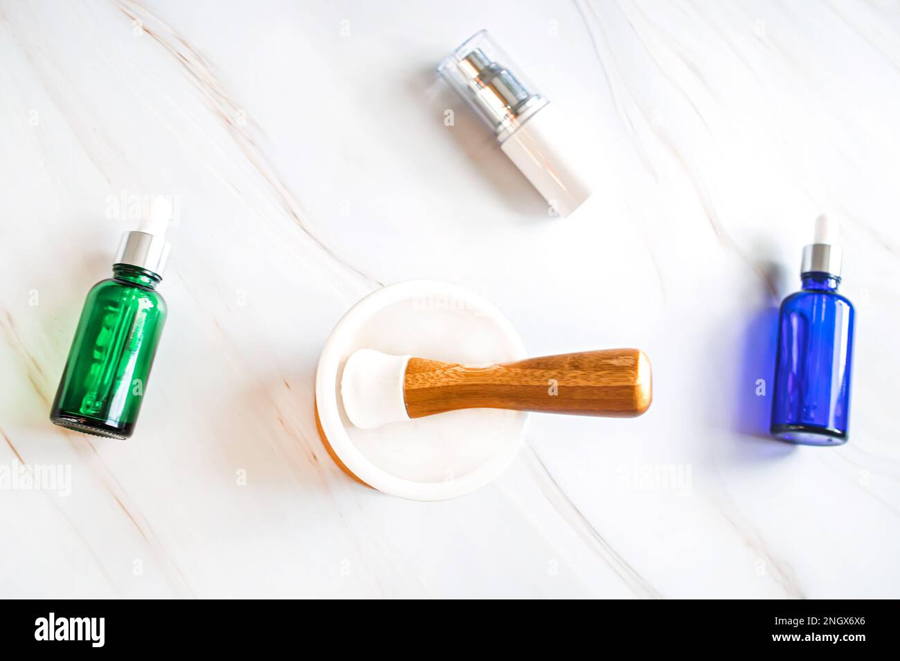 Behälter für Gesichtspflegecremes, Elexiere und ätherische Öle auf einem Marmortisch mit leerem Mörtel für Heilkräuter Stockfoto