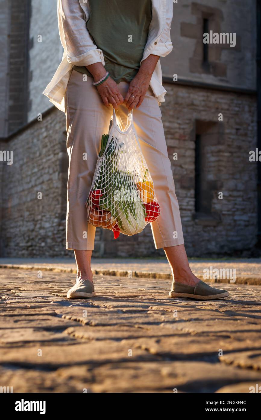 Eine Frau, die auf der Straße steht und eine wiederverwendbare Netztasche mit Gemüse in der Hand hat. Nachhaltiger Lebensstil Stockfoto