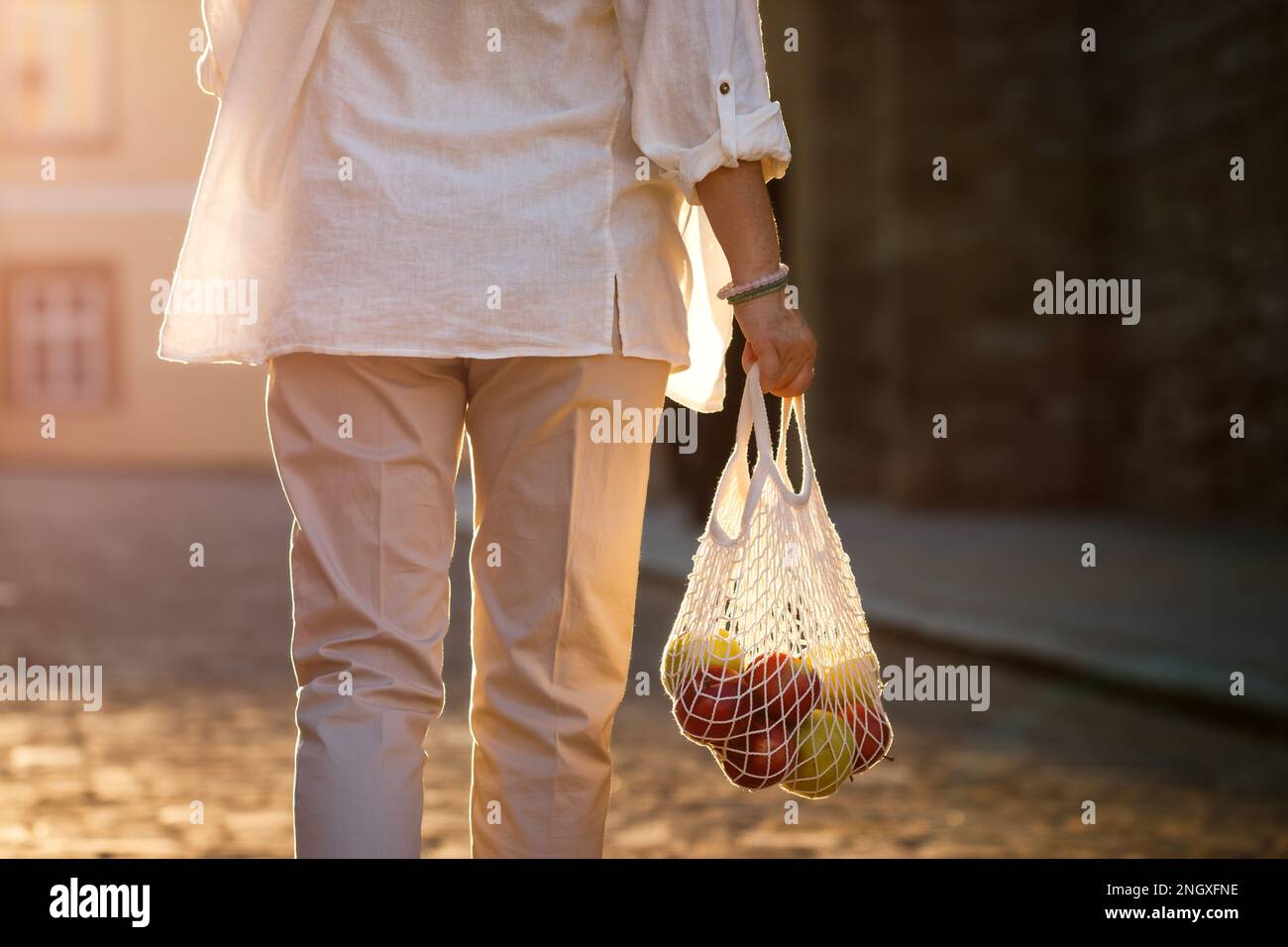 Nachhaltiger Lebensstil. Eine Frau geht auf der Straße und trägt eine wiederverwendbare Netztasche mit Apfelfrüchten Stockfoto