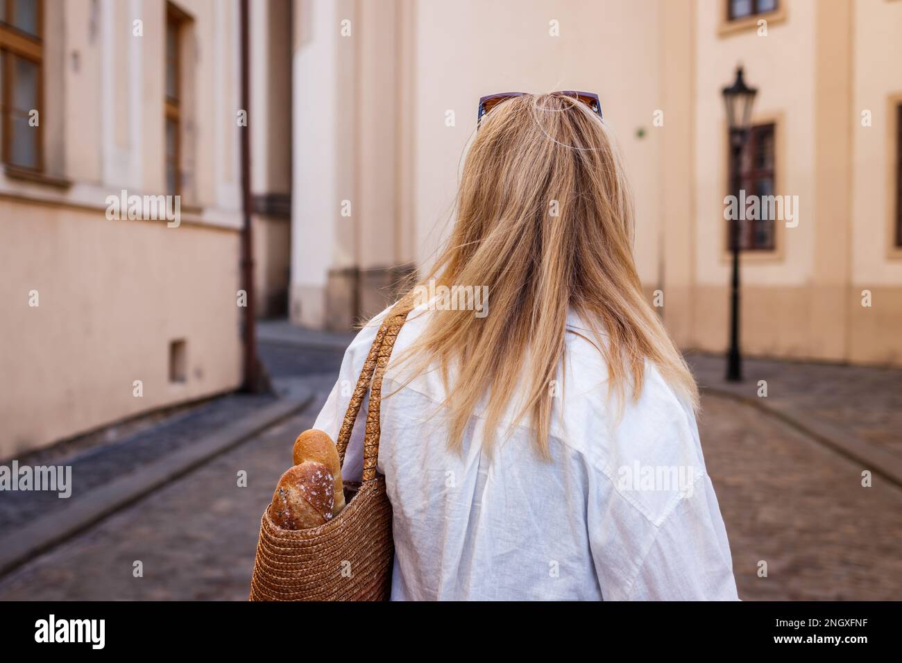 Eine Frau mit wiederverwendbarem Strohsack läuft auf der Straße in der europäischen Altstadt. Nachhaltiger Lebensstil und Stadtleben Stockfoto