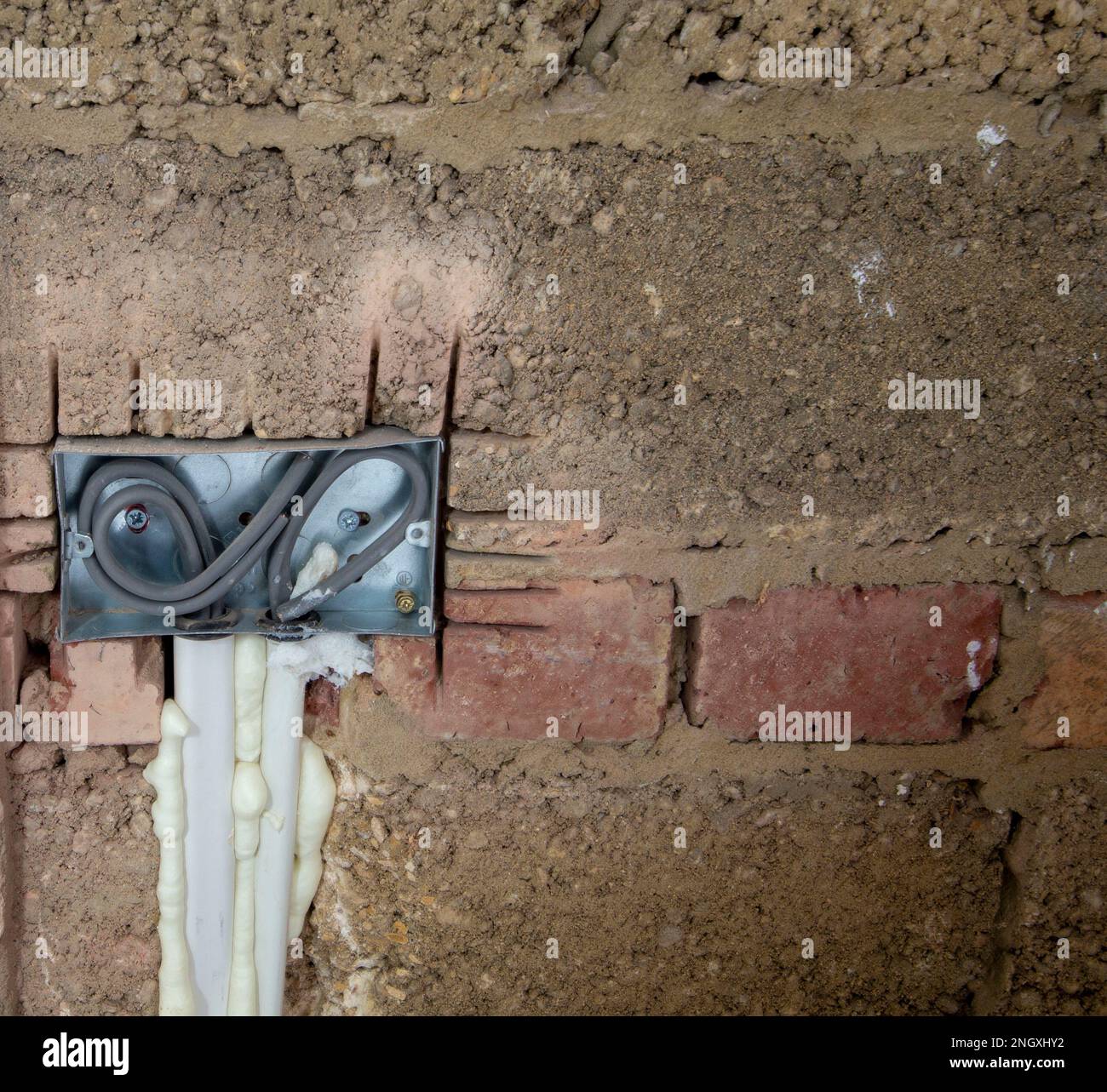 Freiliegende elektrische Leitungen in einer Metallsteckdose, die während Bau- oder Renovierungsarbeiten in einer unfertigen Ziegelwand installiert wurde Stockfoto