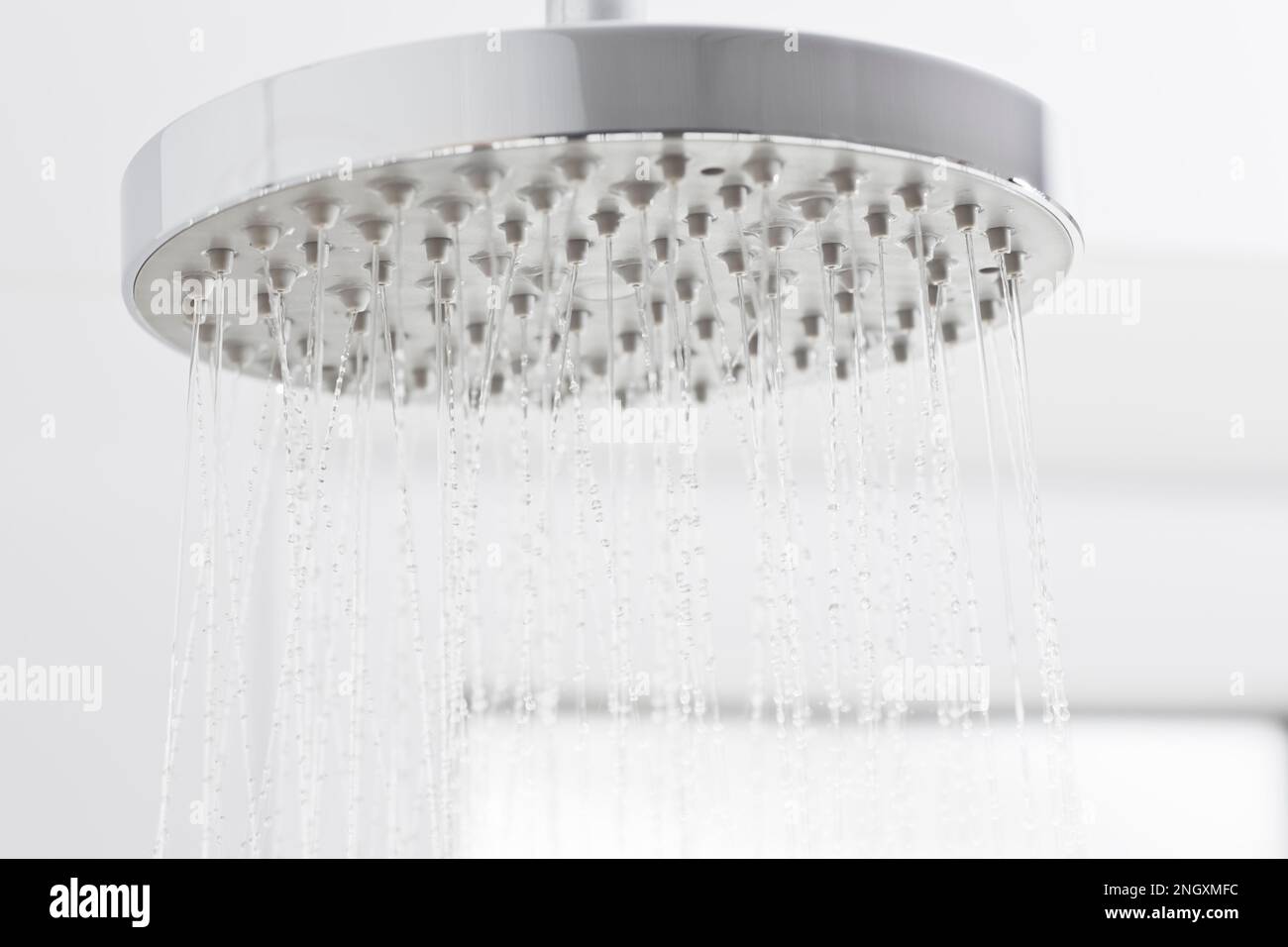 Fließendes Wasser aus einem Duschkopf in einem weißen, hellen Badezimmer - selektiver Fokus Stockfoto