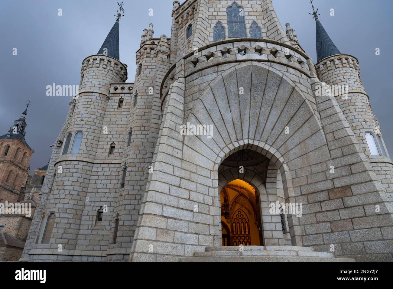 Der Eingang wird von einem warmen Licht erhellt, wenn sich im Episkopalpalast in Astorga, Leon, Spanien Sturmwolken sammeln. Das Wahrzeichen Gebäude von Katalanisch ar Stockfoto