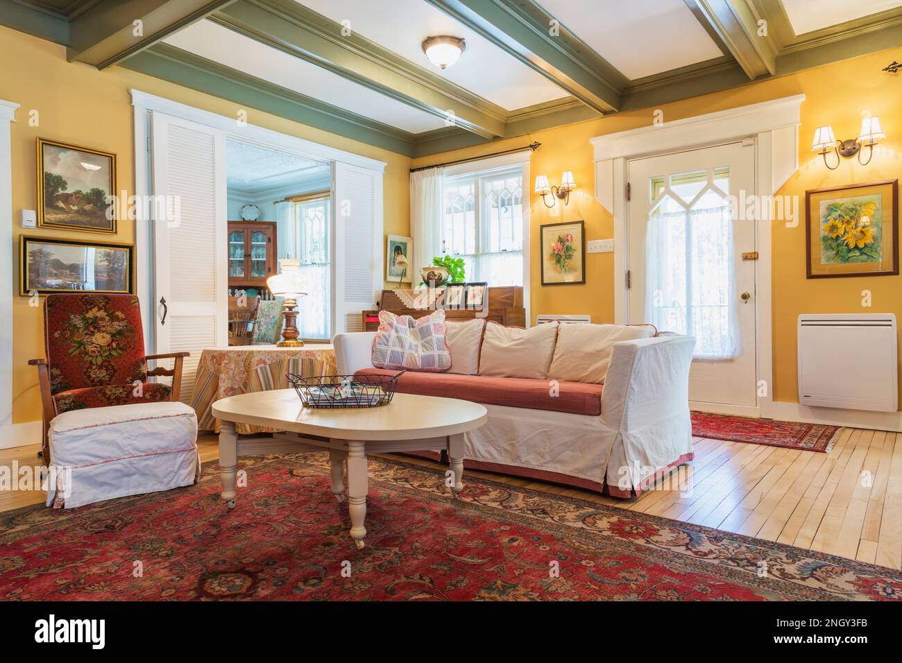 Sofabett aus rotem Samt, gepolsterter Holzsessel, weißer Holztisch im Wohnzimmer mit rotem Teppich und Birkenholzböden. Stockfoto