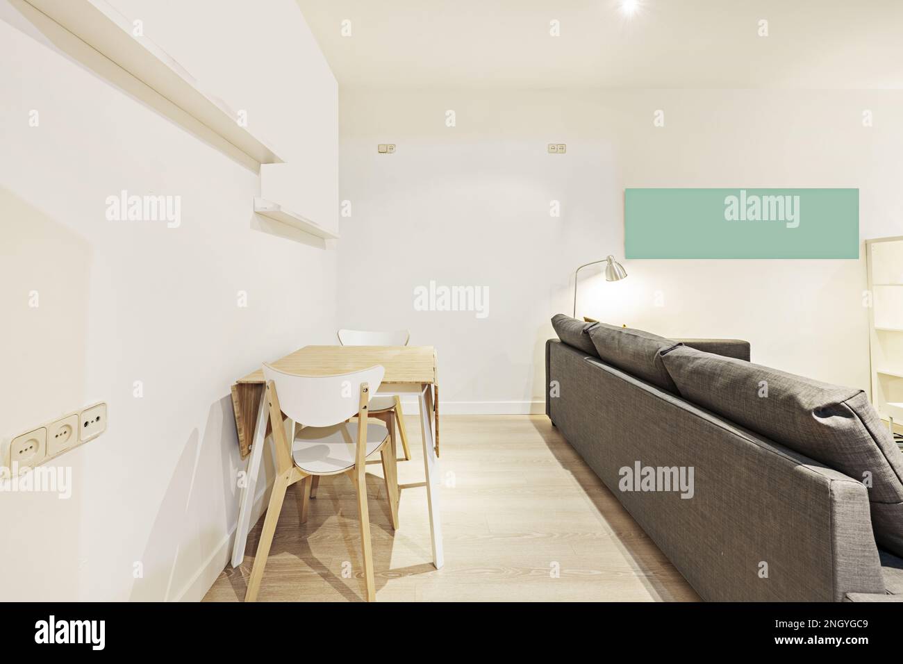 Wohnzimmerecke mit großem grauen Stoffsofa und Holzfalttisch mit weißem Rahmen und passenden Stühlen Stockfoto