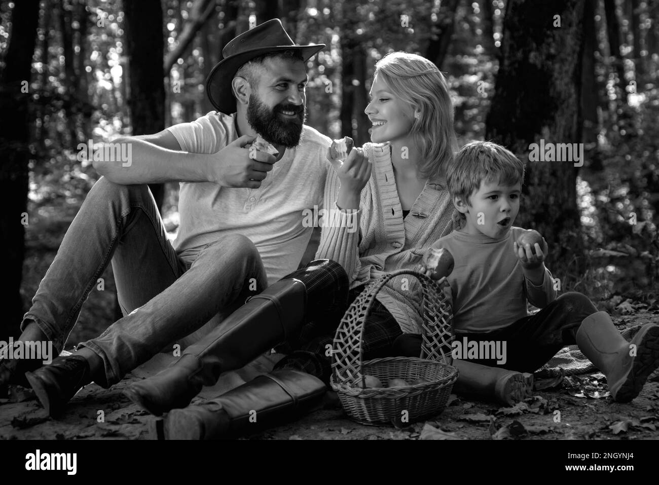 Fröhliche Familie sitzt auf dem Gras während eines Picknicks in einem Park. Junge lächelnde Familie macht ein Picknick an einem Herbsttag. Glückliche Familie im Park Stockfoto