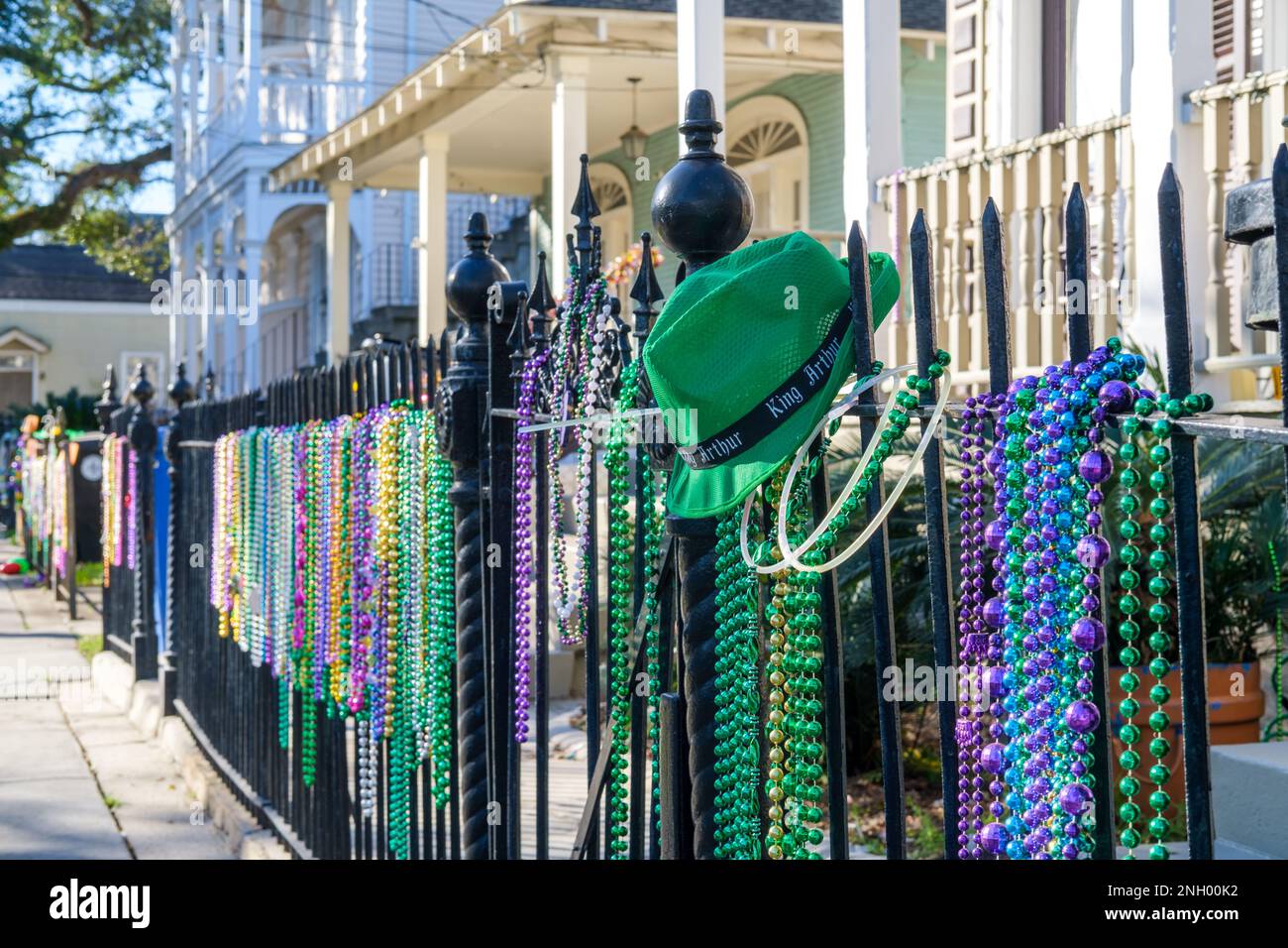 NEW ORLEANS, LA, USA - 13. FEBRUAR 2023: Selektivfokus des grünen Krewe of King Arthur hat auf einem eisernen Zaun mit Mardi Gras Perlen und Wohnhäusern in Uptown Stockfoto