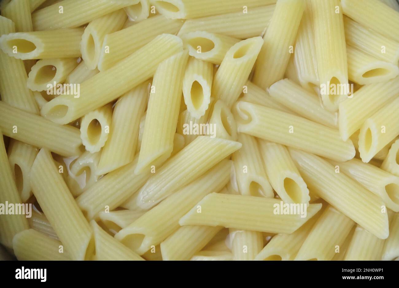 Speisen und Küche, Penne Pasta in heißem Wasser, Eine vielseitige röhrenförmige italienische Pasta, perfekt für verschiedene Gerichte mit Saucen und Zutaten. Stockfoto
