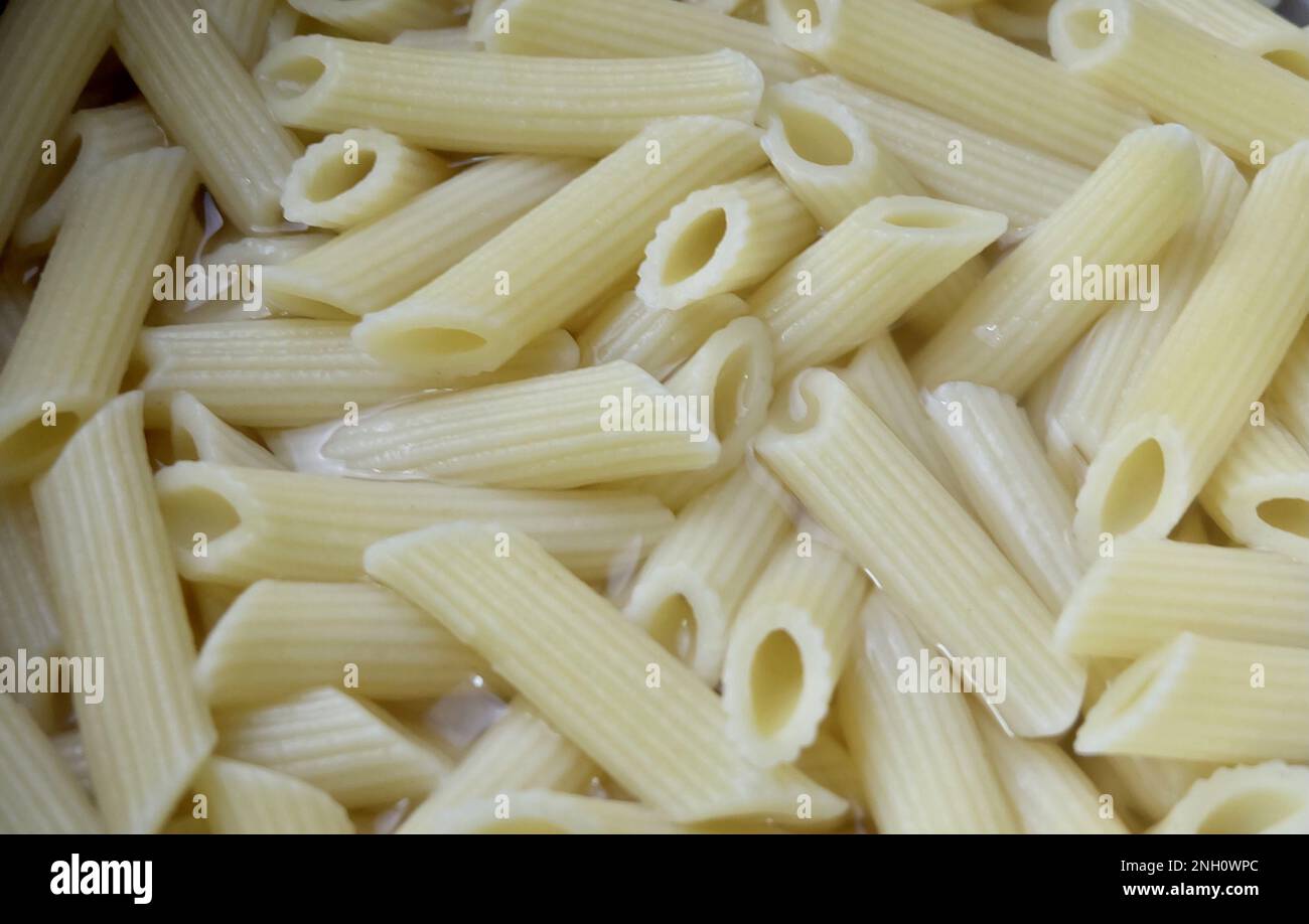 Speisen und Küche, Penne Pasta in heißem Wasser, Eine vielseitige röhrenförmige italienische Pasta, perfekt für verschiedene Gerichte mit Saucen und Zutaten. Stockfoto